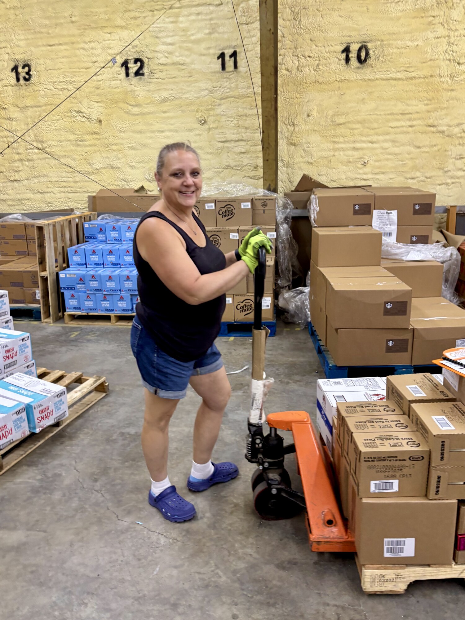 A volunteer maneuvers a pallet jack loaded with boxes of dressing and pantry staples into position alongside other prepared pallets.