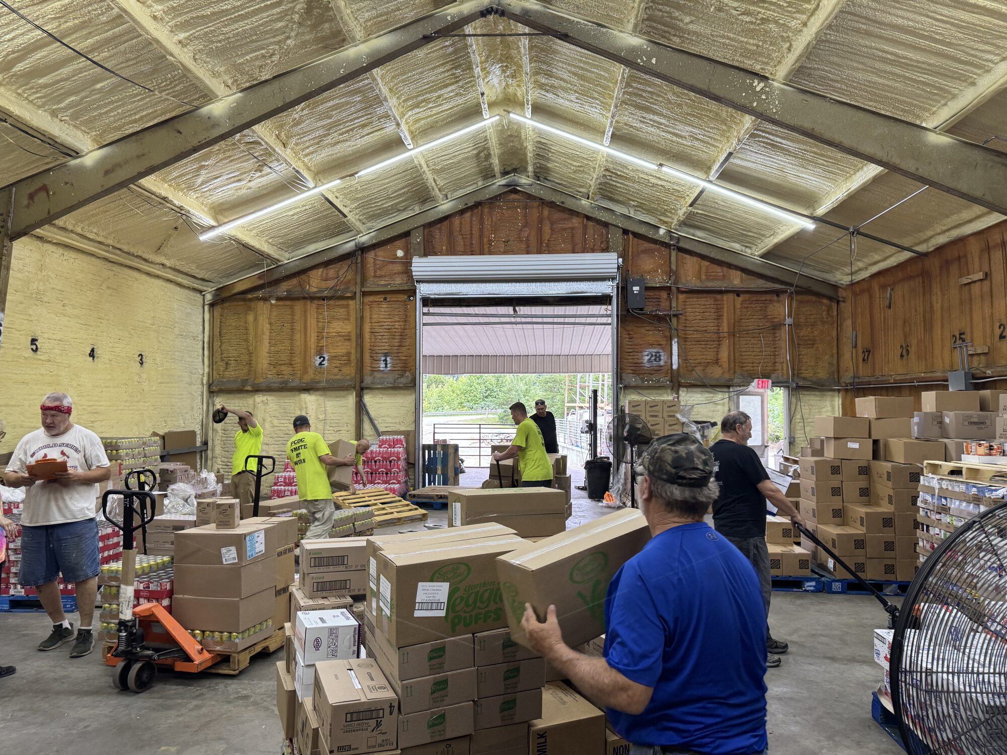 Volunteers move boxes of pantry staples through the Clay City warehouse, staging pallets near the open loading bay for the next distribution.